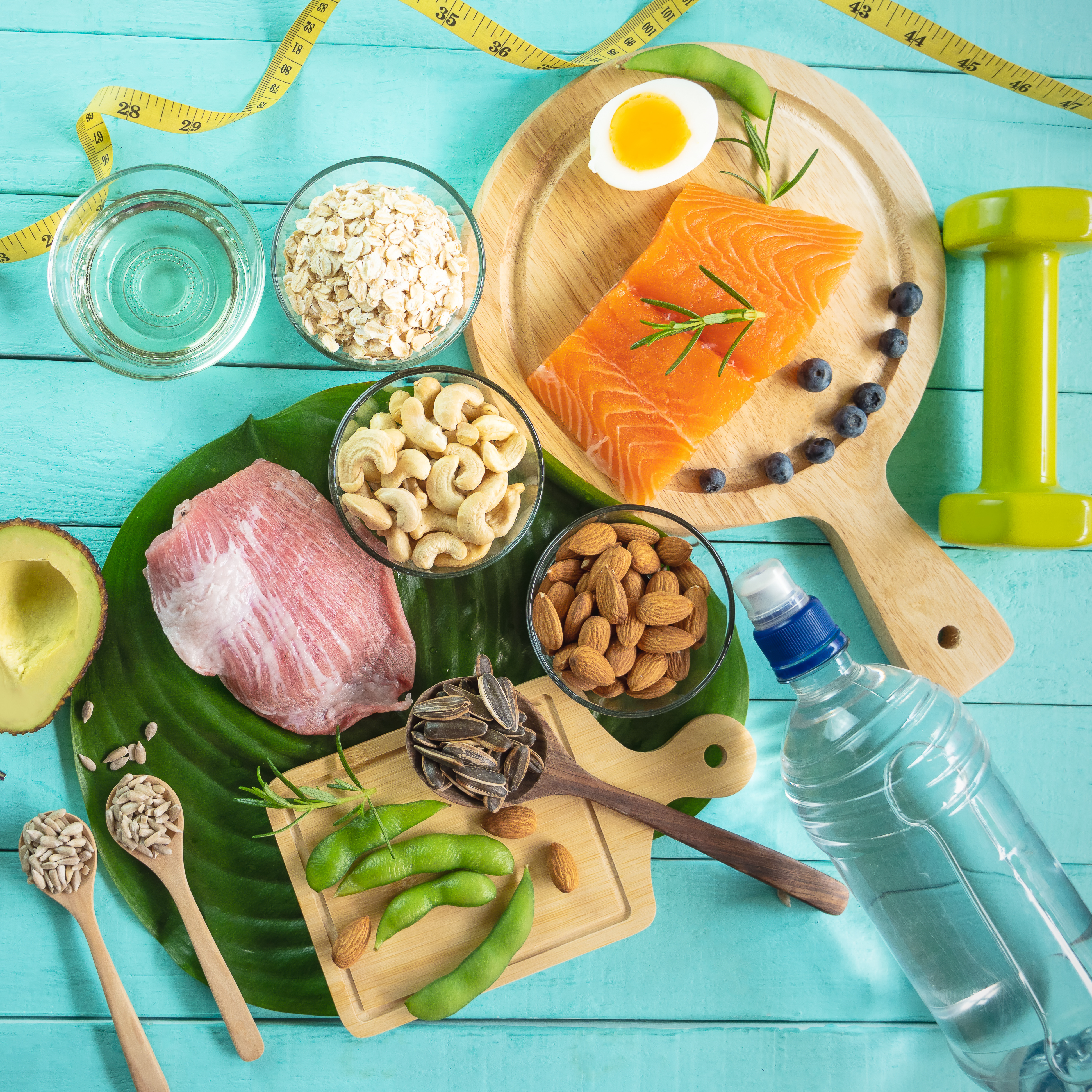 Assortment of healthy foods like fish, nuts, vegetables, and water alongside a dumbbell and a measuring tape, symbolizing functional medicine and holistic wellness.